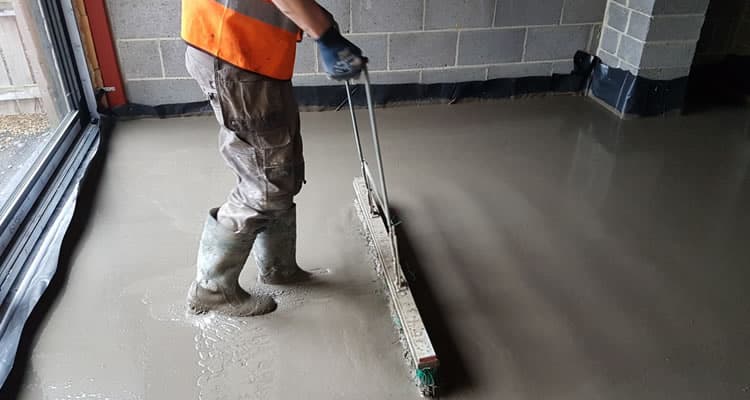 A flowing screed being levelled across a floor with a dappling bar before it sets