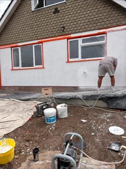 A DSL Plastering renderer working a fresh coat into a house wall, windows masked off and the render pump running below