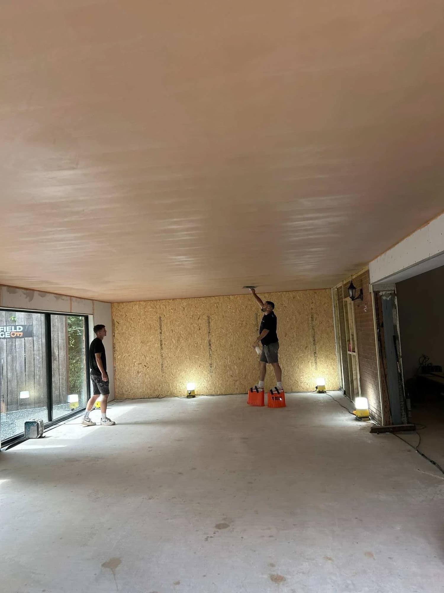 A DSL Plastering team finishing a freshly skimmed ceiling across a large extension, work lights raking across the flat surface